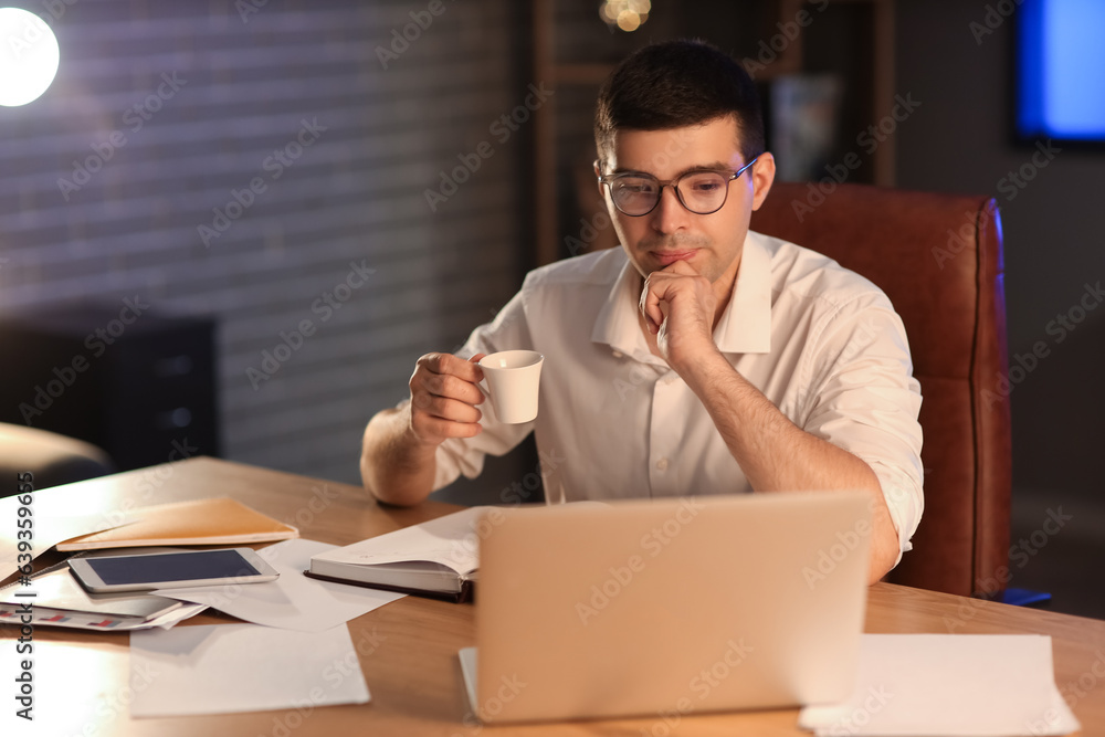 Young businessman with cup of coffee working in office at night