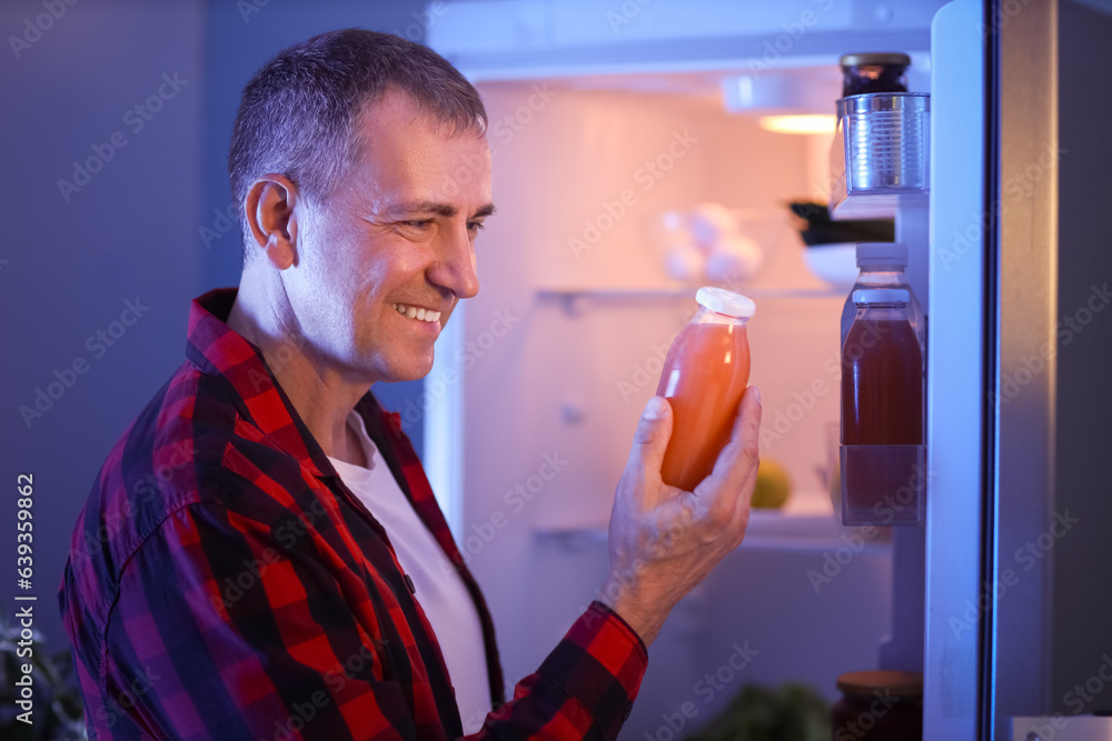 Mature man with bottle of juice near open fridge in kitchen at night, closeup