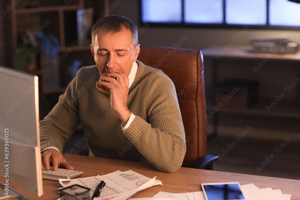 Mature man eating burger in office at night