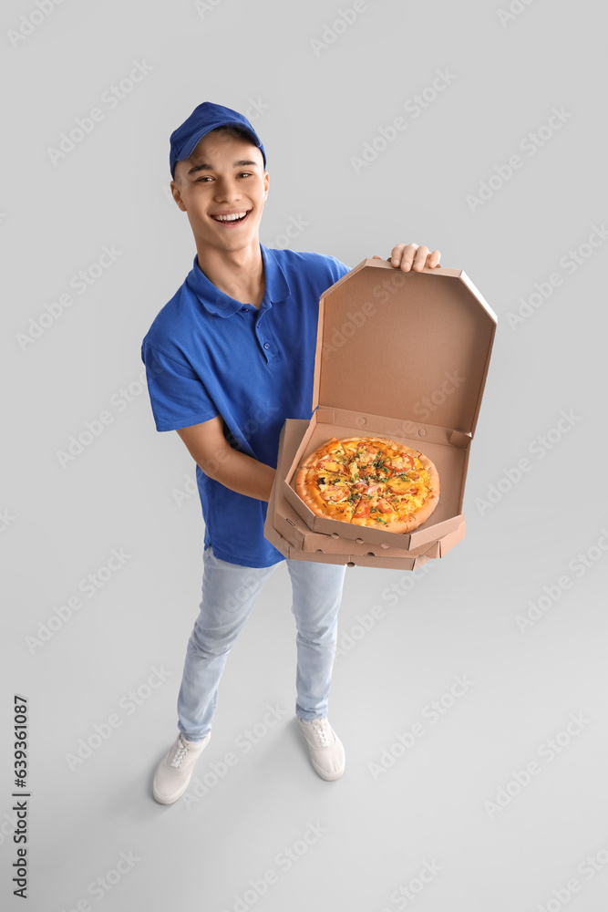 Young courier with pizza on light background