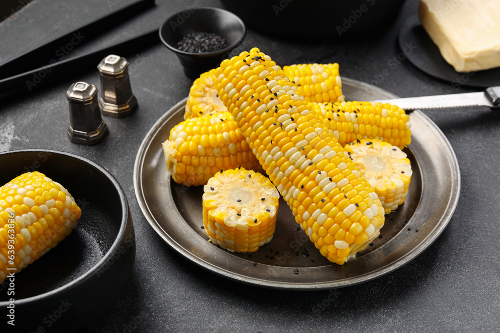 Plate and bowl with boiled corn cobs on black background