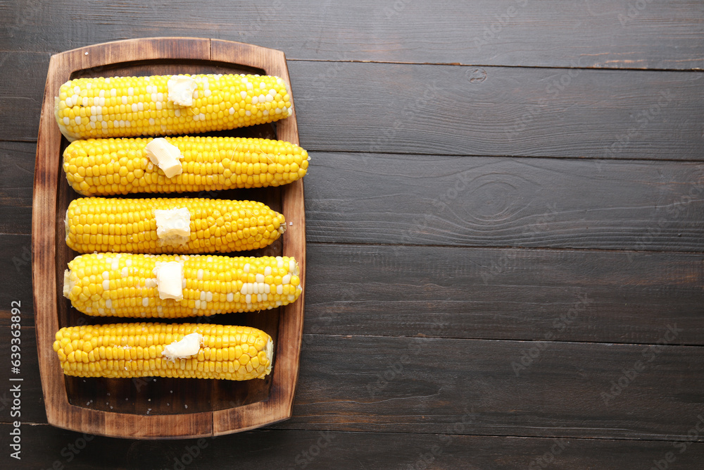 Board of boiled corn cobs with butter on wooden background