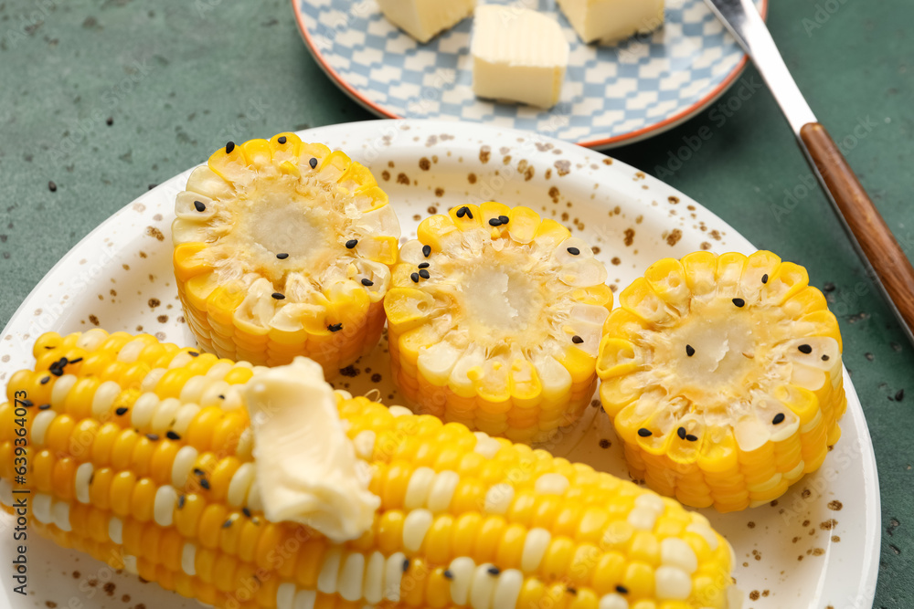 Plate of boiled corn cobs with butter on green background