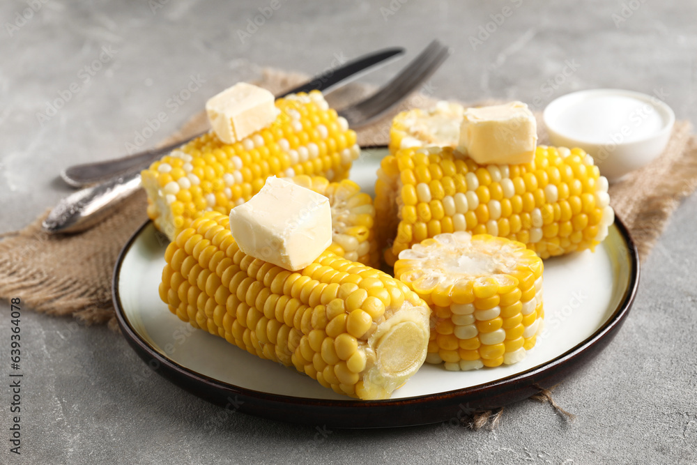 Plate of boiled corn cobs with butter on grey background