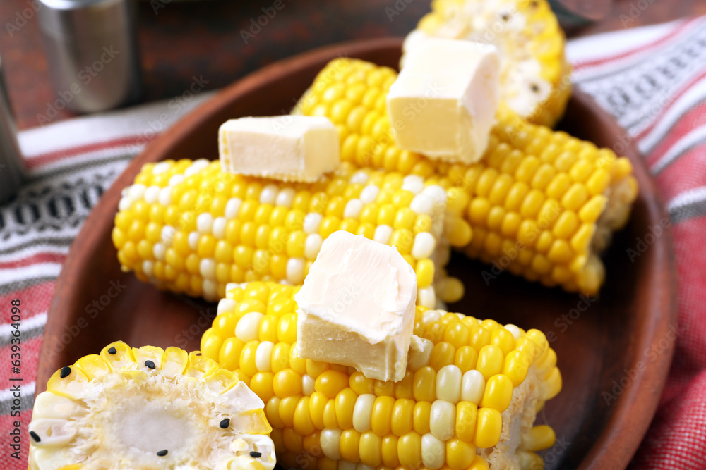 Plate of boiled corn cobs with butter on dark background