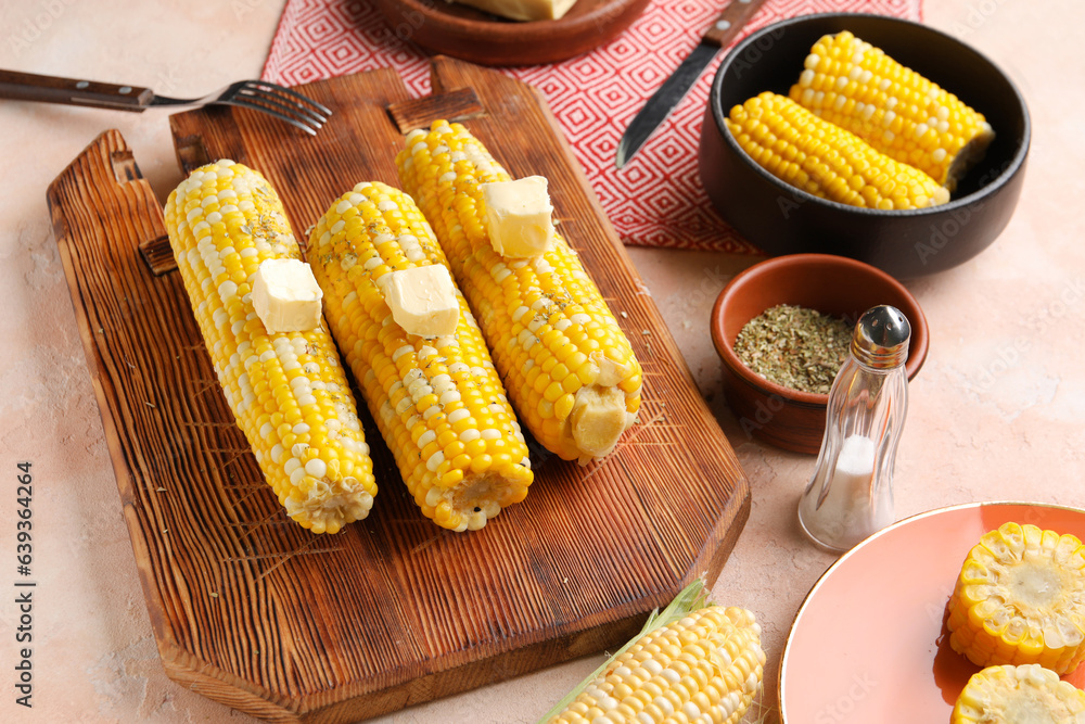 Wooden board of boiled corn cobs with butter on pink background