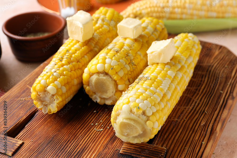 Wooden board of boiled corn cobs with butter on pink background, closeup