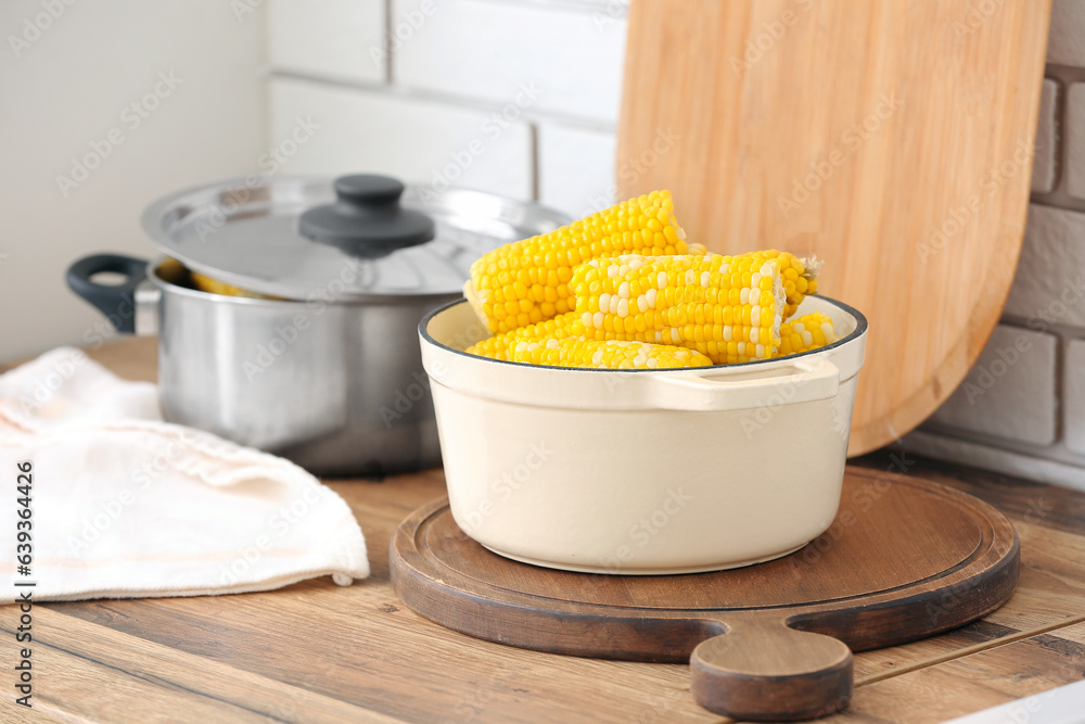 Cooking pot with boiled corn cobs on wooden table in kitchen