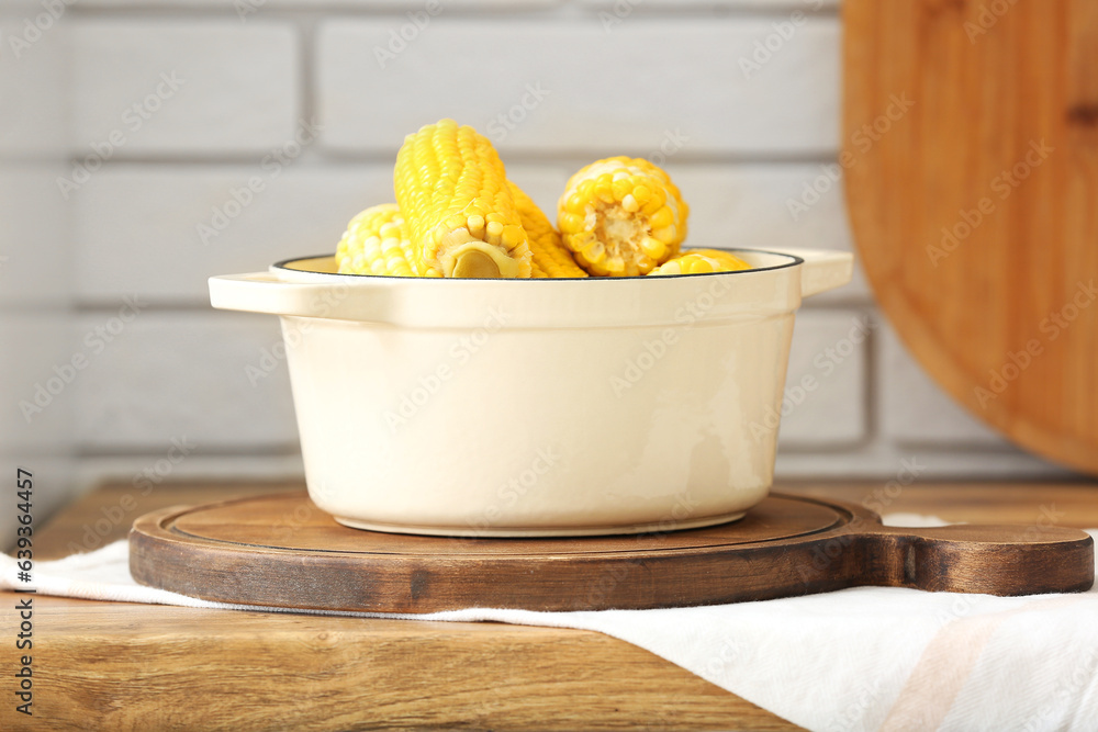 Cooking pot with boiled corn cobs on wooden table in kitchen