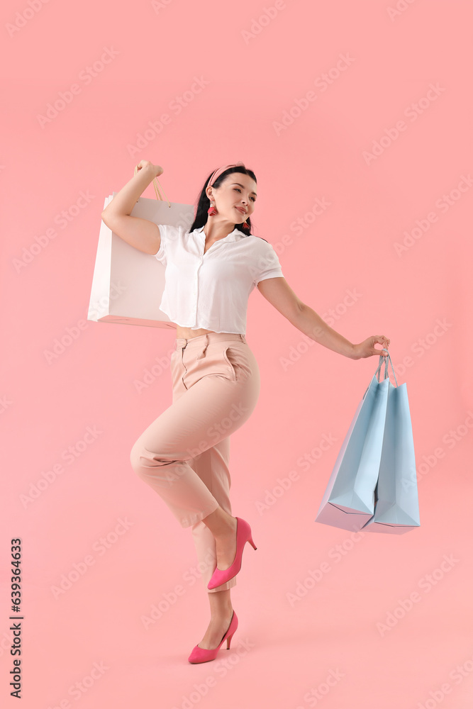 Portrait of happy young woman with shopping bags on pink background