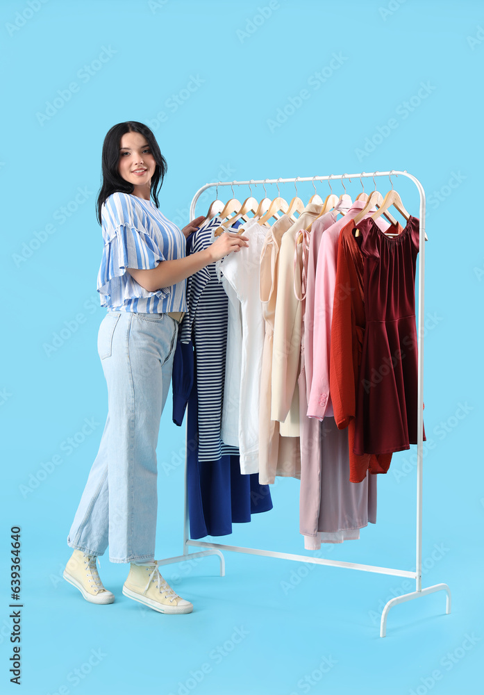 Beautiful young woman choosing clothes on blue background