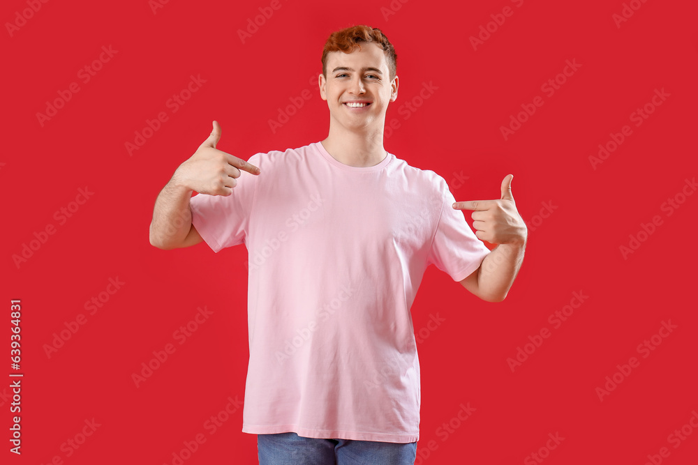 Young man pointing at his t-shirt on red background