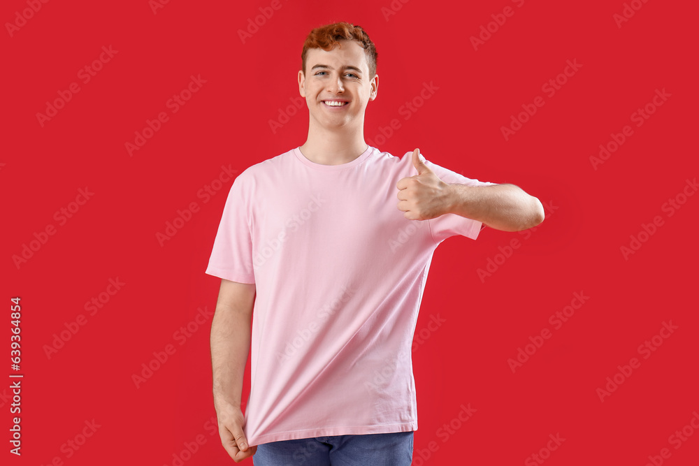 Young man in t-shirt showing thumb-up on red background