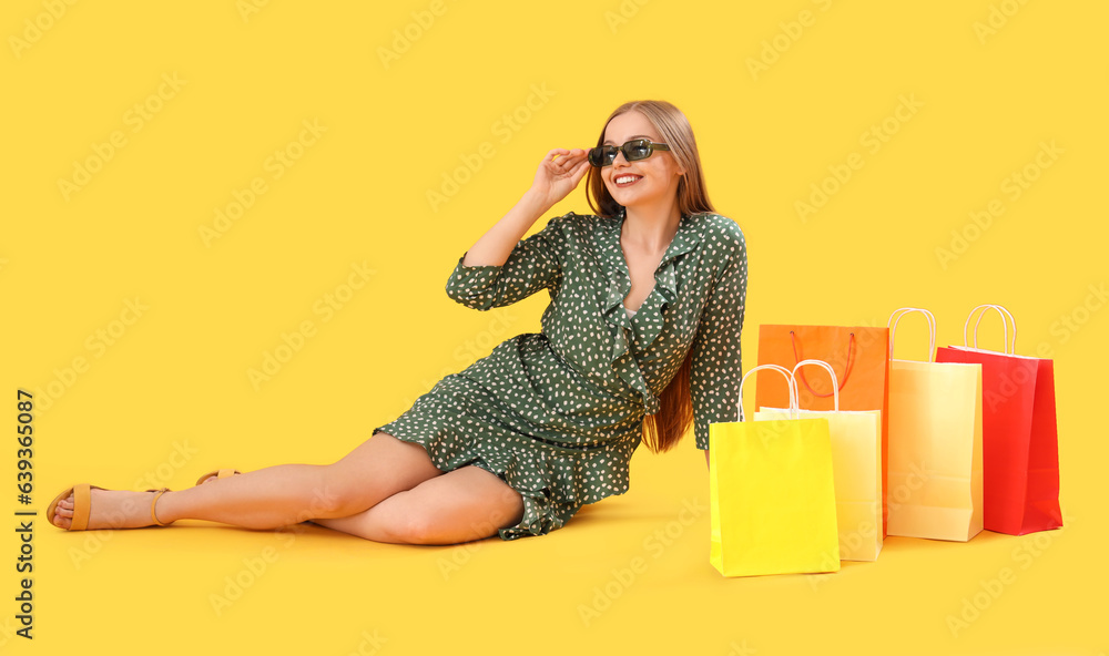 Pretty young woman sitting near shopping bags on orange background