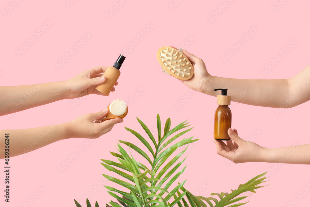 Female hands holding cosmetic products with palm leaves on pink background