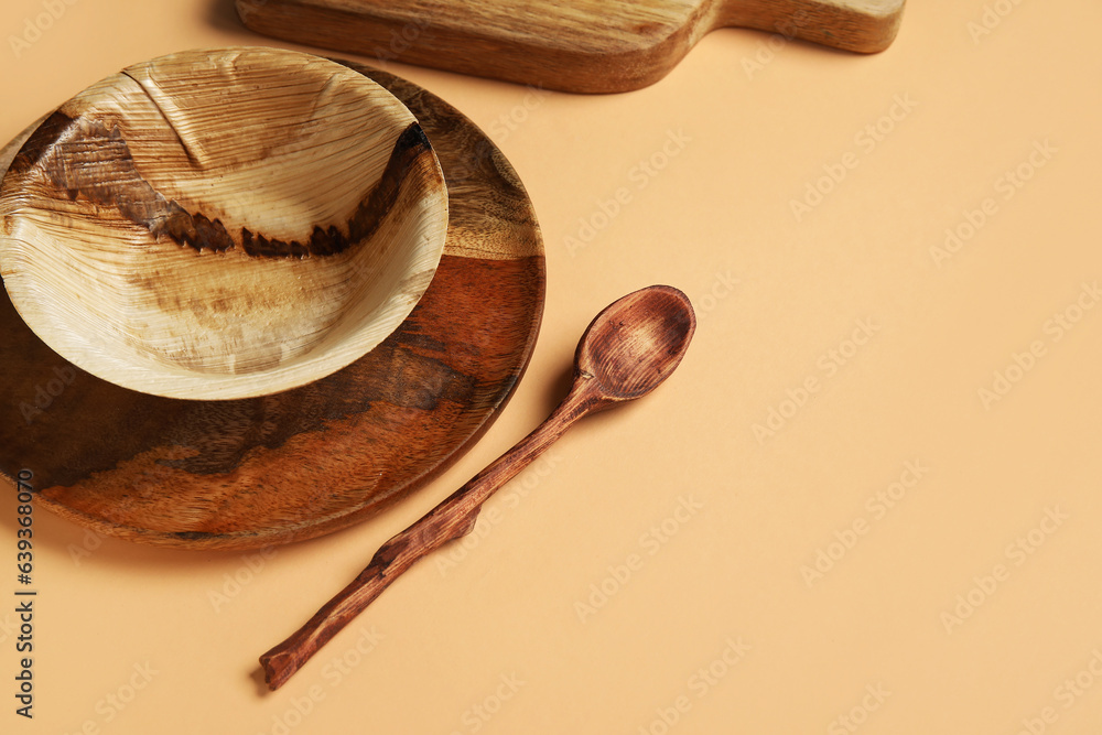 Wooden plate, bowl and spoon on beige background, closeup