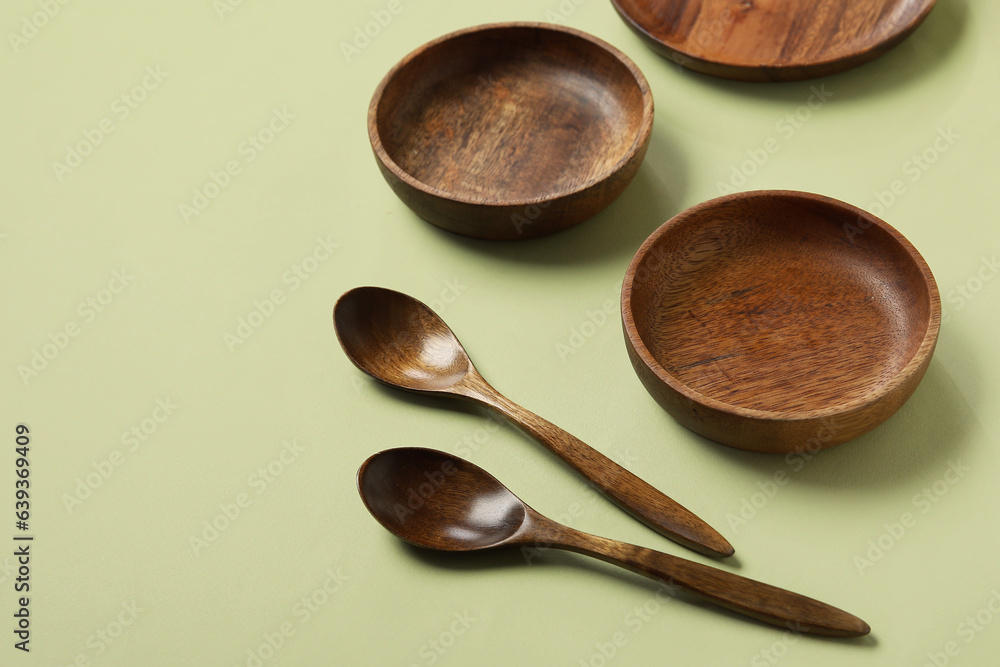 Wooden plates and spoons on green background, closeup