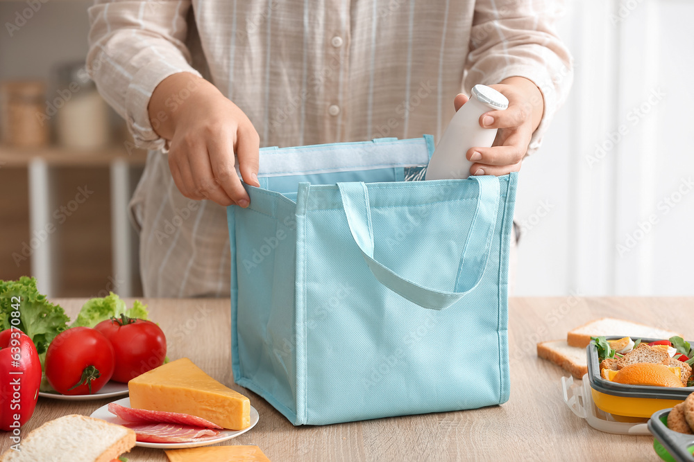 Mother packing drink into lunch box bag in kitchen