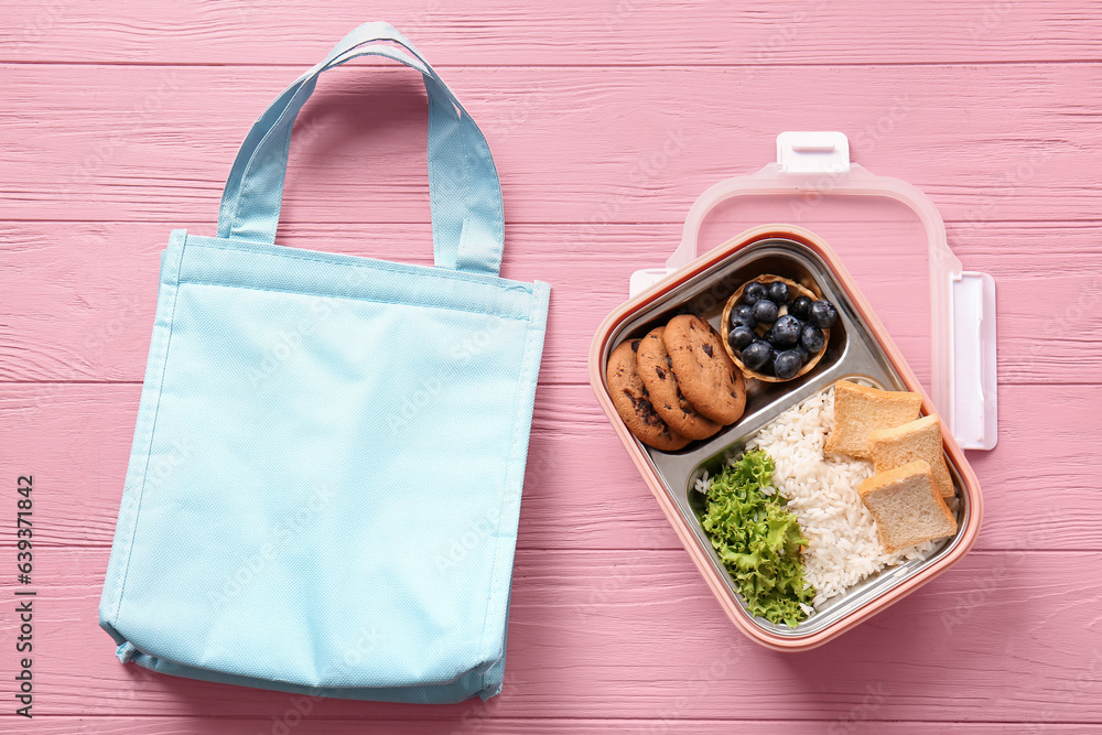 Bag and lunchbox with delicious food on pink wooden background