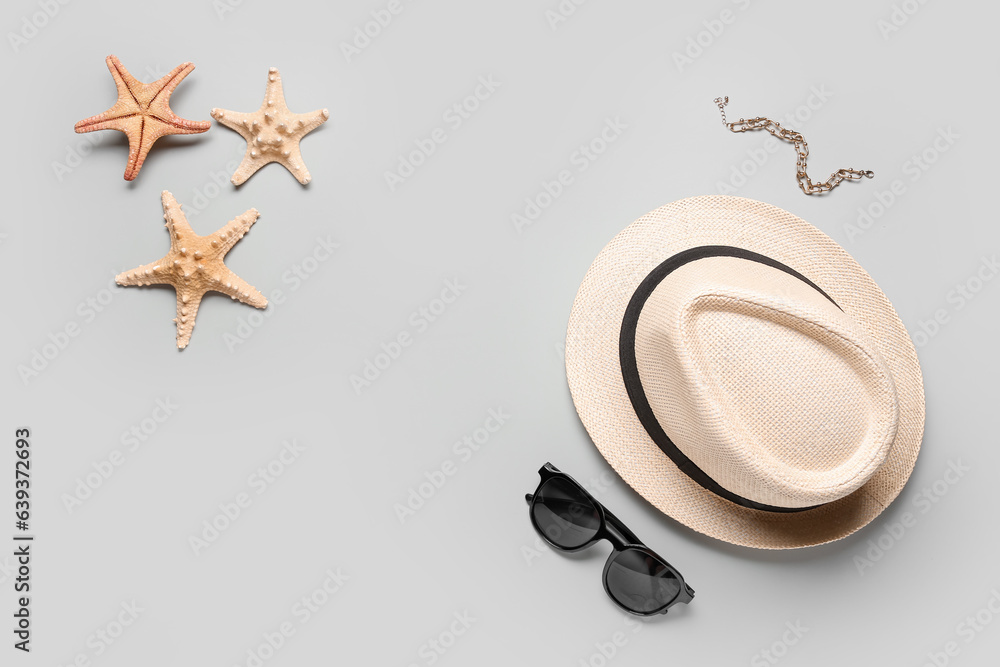 Composition with stylish hat, bracelet, sunglasses and starfishes on grey background