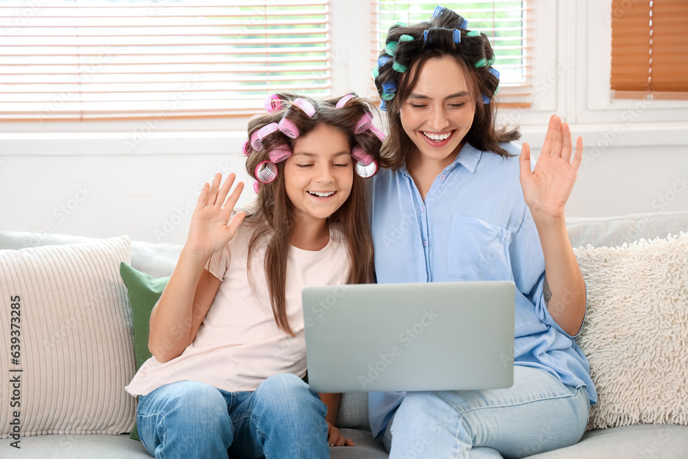 Little girl and her mother with hair curlers using laptop at home