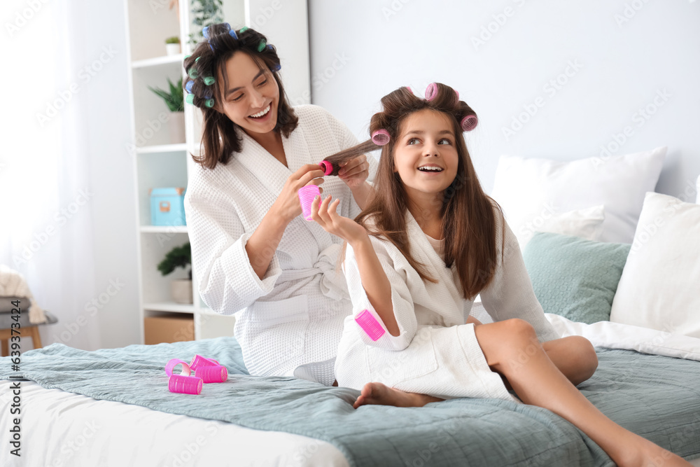 Little girl with her mother curling hair in bedroom