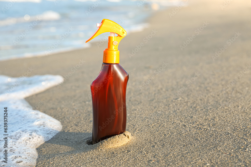 Bottle of sunscreen cream on sand near ocean at beach