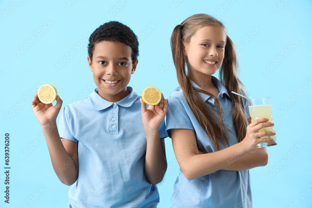 Little children with glass of fresh citrus juice and lemon slices on blue background