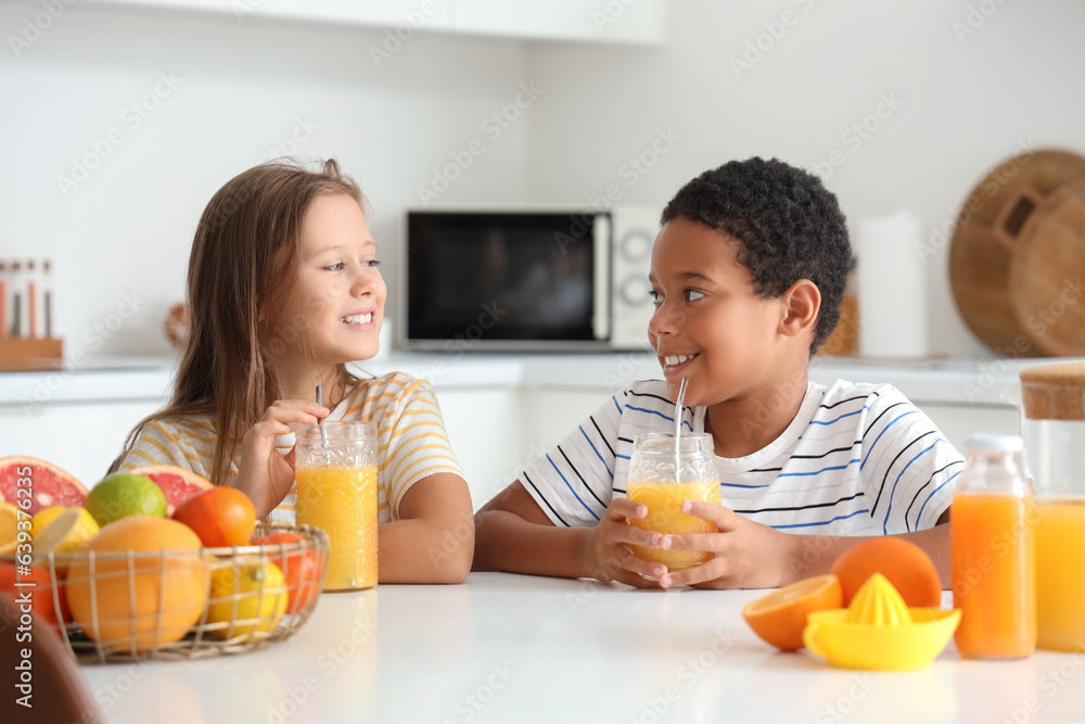 Little children with glasses of fresh citrus juice sitting at table in kitchen