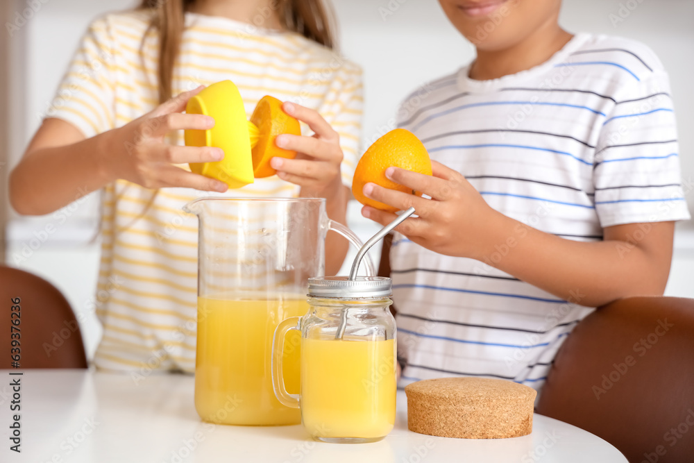 Little children making fresh orange juice at table in kitchen