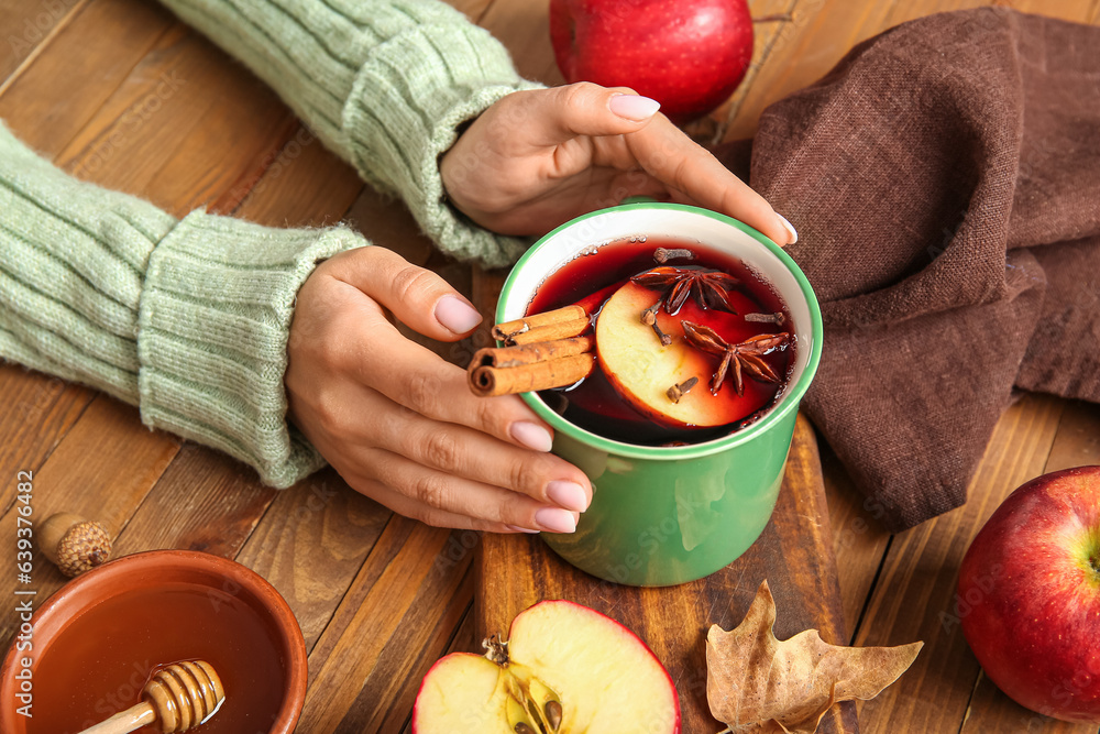 Female hands with cup of hot mulled wine and apple on wooden background