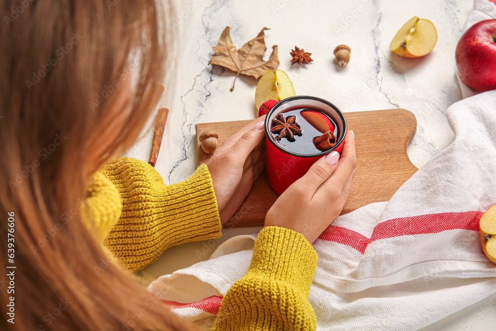 Woman holding cup of hot mulled wine with apple and cinnamon on white background