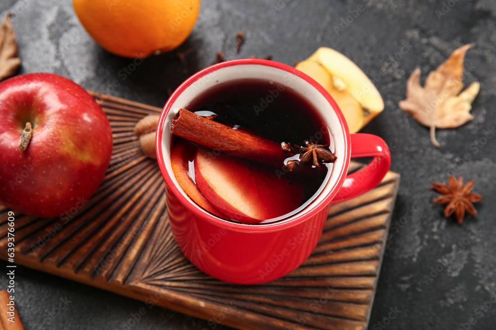 Cup of hot mulled wine with apple and orange on black background