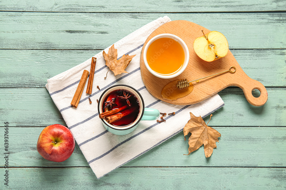 Cup of hot mulled wine with apple and bowl of honey on green wooden background