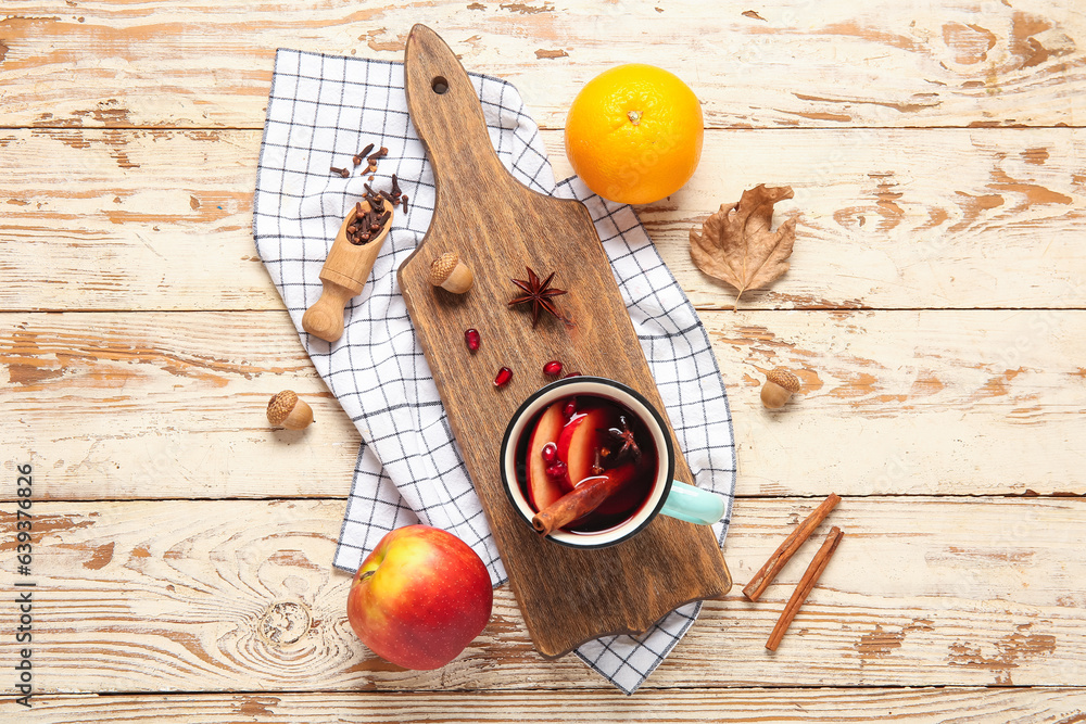 Cup of hot mulled wine with apple and pomegranate on white wooden background