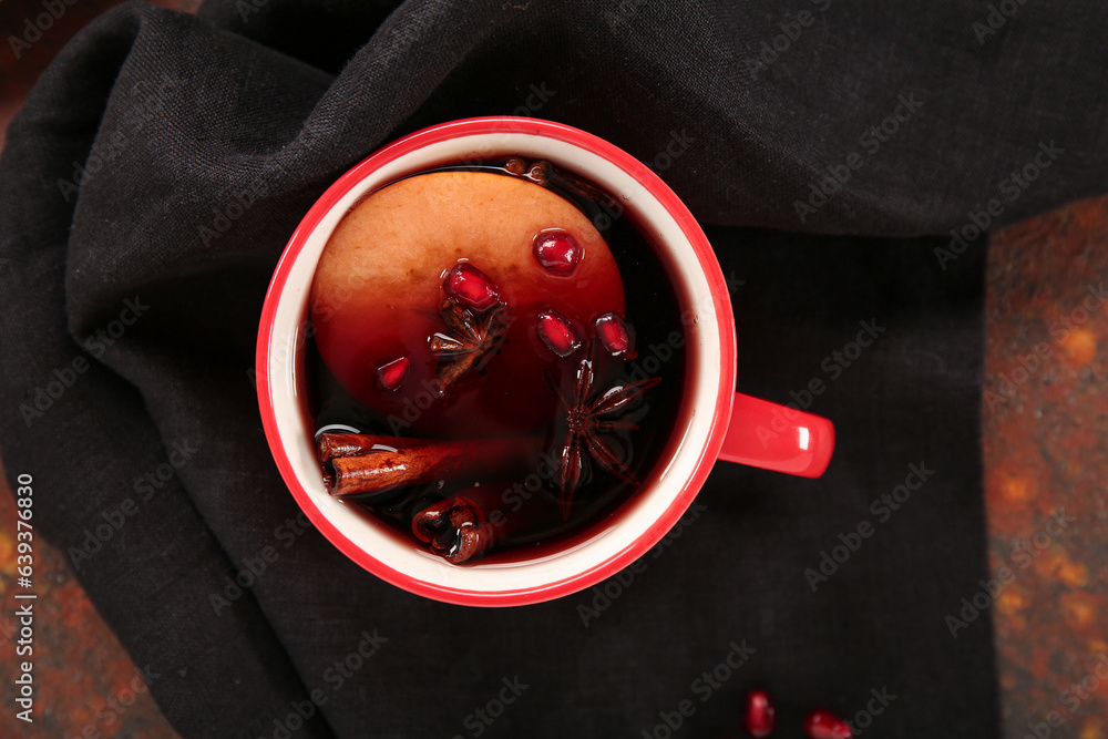 Cup of hot mulled wine with pomegranate and apple on dark background