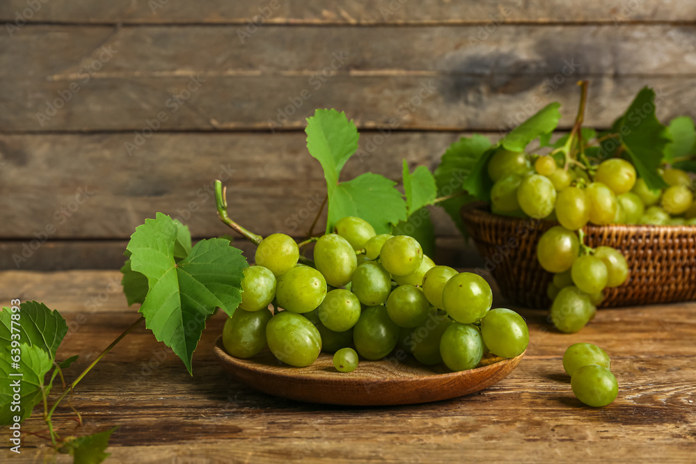 Plate and wicker bowl with sweet green grapes on wooden background