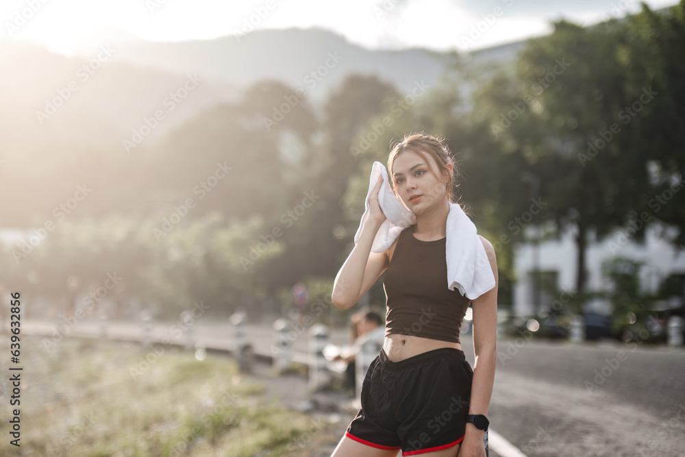 Portrait Young beautiful Asian woman wiping sweat after evening jogging in the park.