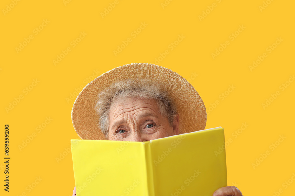 Senior woman reading book on yellow background, closeup