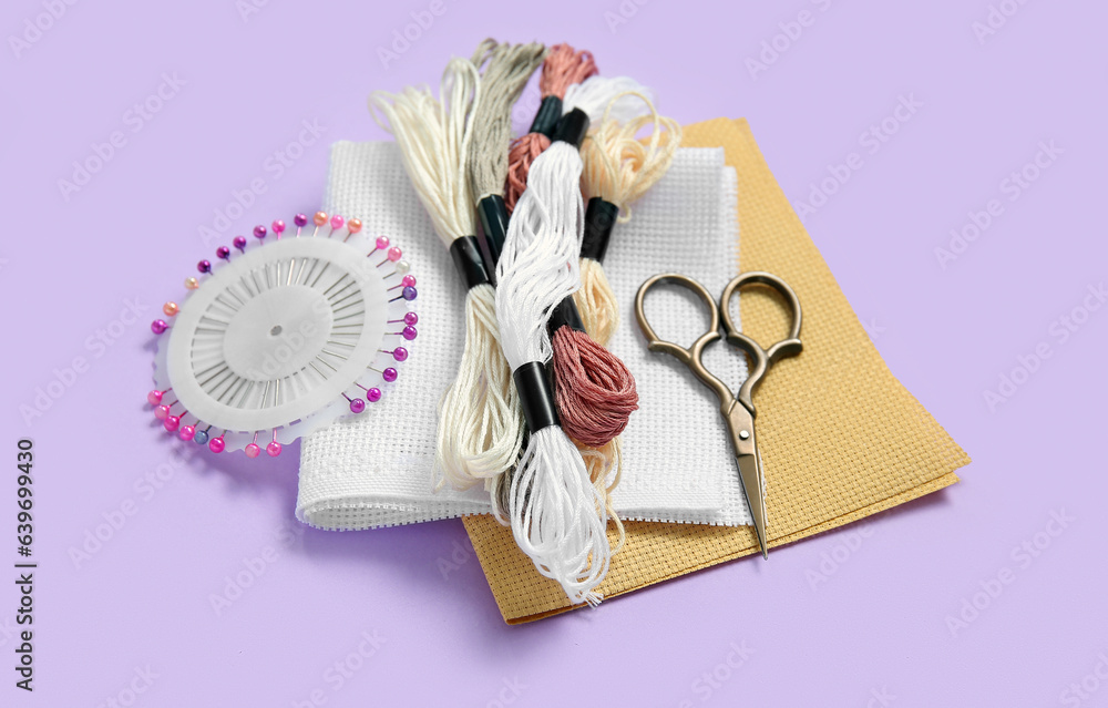 Different canvases with scissors, mouline threads and ball pins on lilac background