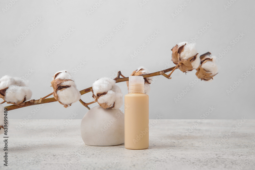 Bottle of cosmetic product, plaster podium and cotton branch on light background