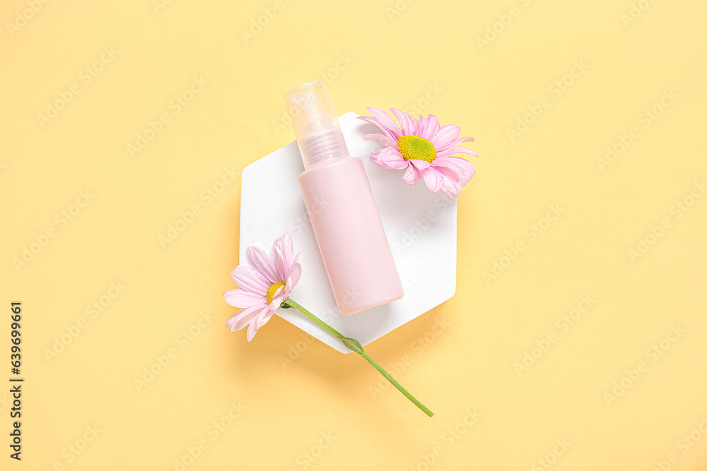 Plaster podium with bottle of cosmetic product and beautiful flowers on color background