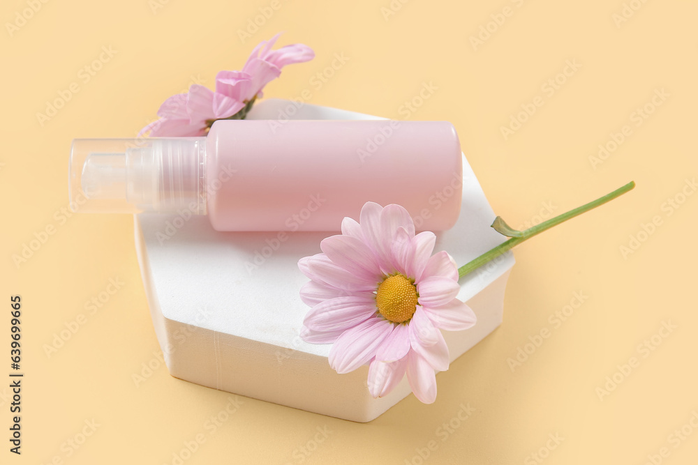 Plaster podium with bottle of cosmetic product and beautiful flowers on color background