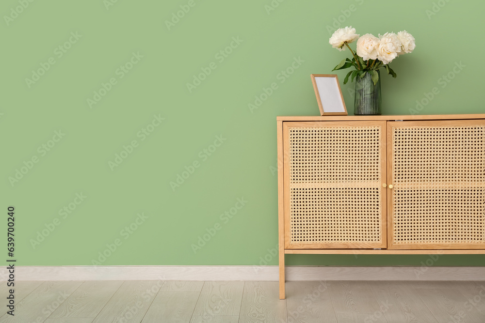 Vase of white peonies and photo frame on dresser near green wall