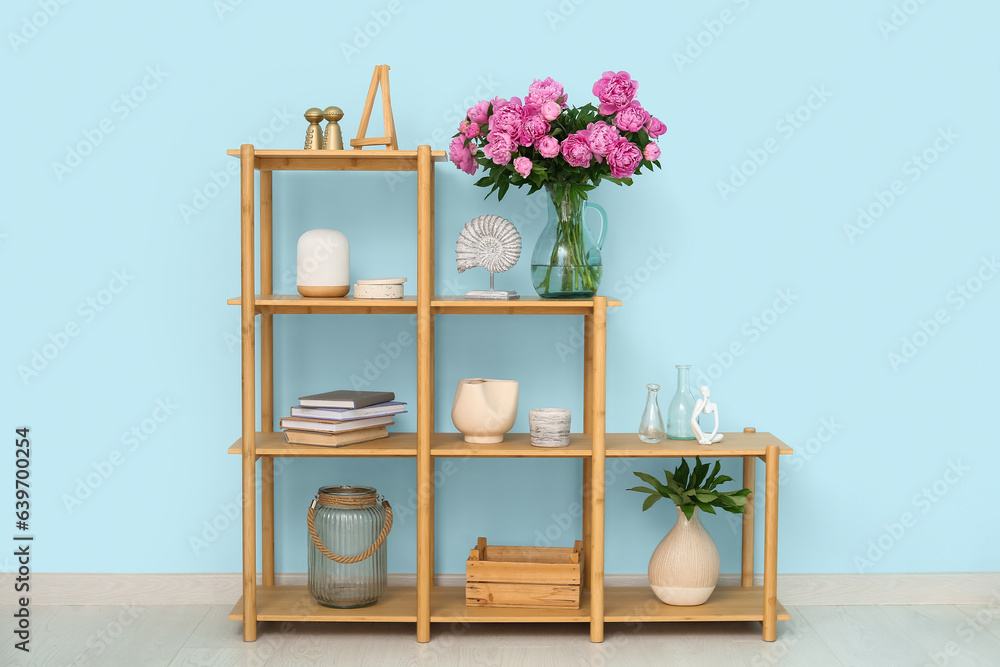 Vase of pink peonies on shelving unit near blue wall