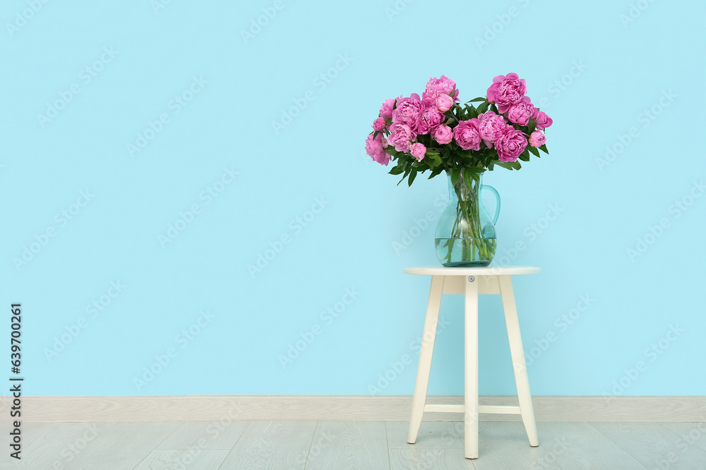 Vase of pink peonies on chair near blue wall