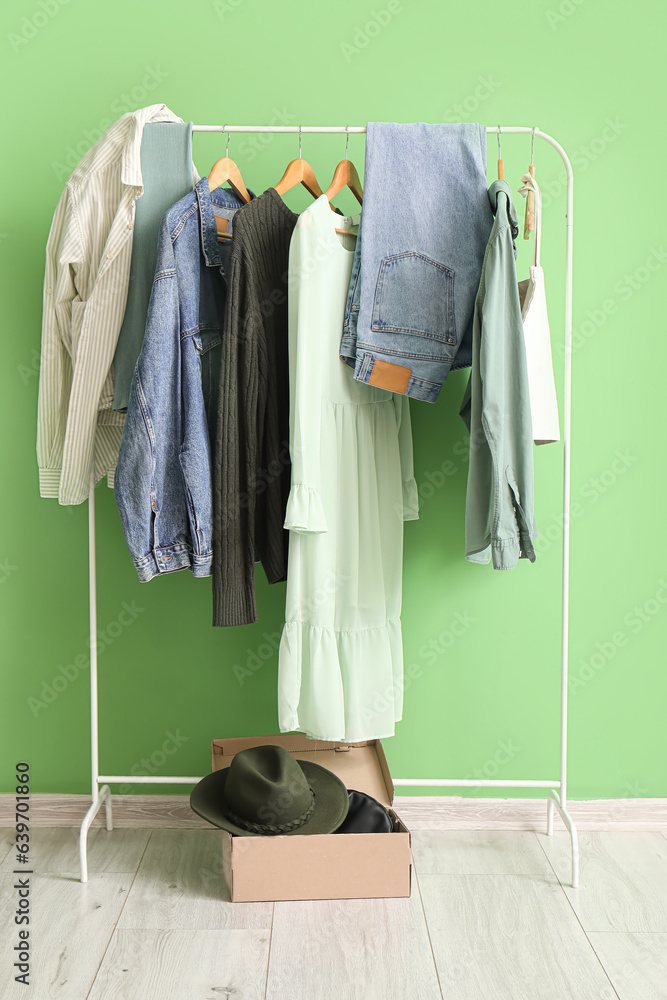 Stylish clothes hanging on rack and box with accessories against green wall