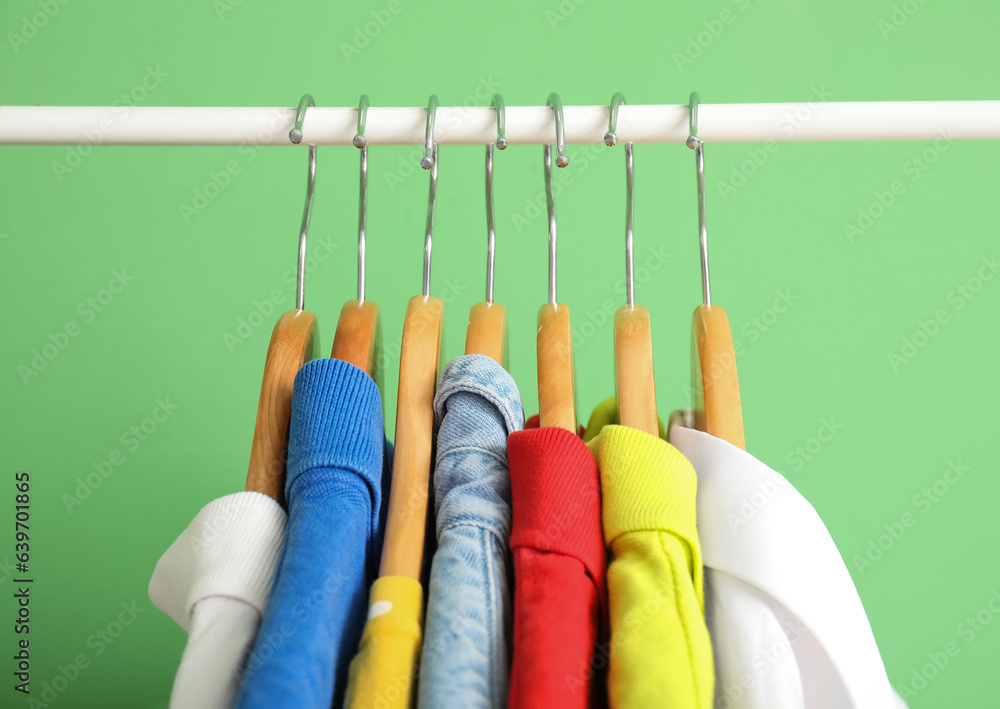 Different clothes hanging on rack against green wall, closeup