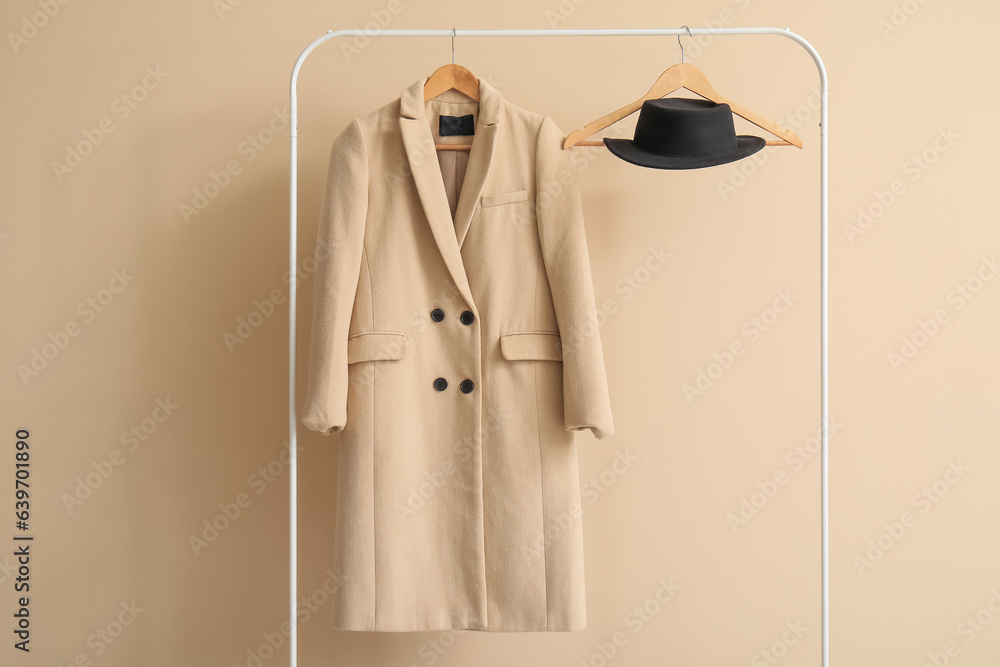 Stylish coat and hat hanging on rack against color wall