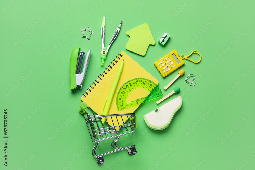 Composition with shopping cart and different stationery on green background